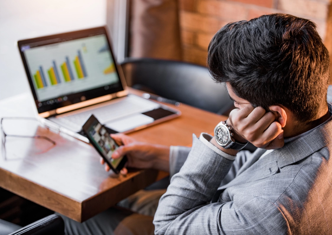 Business professional frustrated with database slowness issues while analyzing performance charts on laptop and mobile device